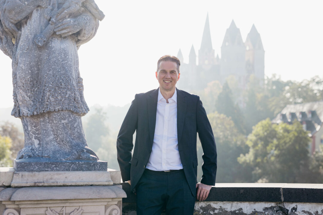 Gunnar Johannen steht neben einer Statue und im Hintergrund sieht man ein Schloss.