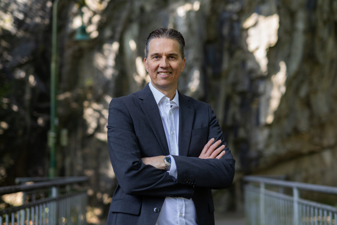 Gunnar Johannen steht mit verschränkten Armen da. Er trägt eine Armbanduhr, ein dunkelblaues Jackett und ein hellblaues Hemd.