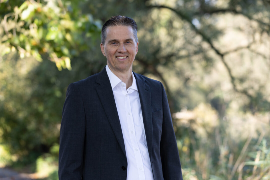 Gunnar Johannen steht draußen in der Natur. Er trägt ein dunkelblaues Jacket und darunter ein helles Hemd.
