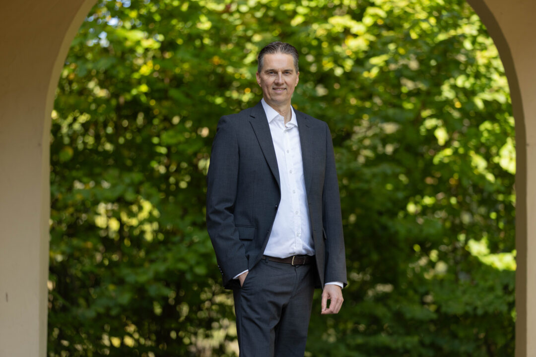 Gunnar Johannen steht mit einem dunkelblauen Anzug und einem hellen Hemd in der Natur.