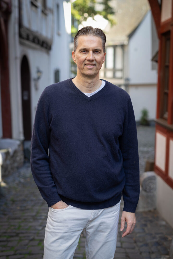 Gunnar Johannen steht in einer Gasse. Er trägt einen dunkelblauen Pullover und eine weiße Hose.